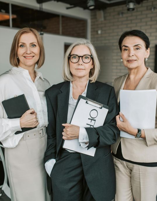 Group of senior female professionals confidently posing in office setting.