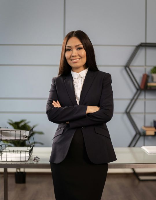 Portrait of a smiling professional woman in formal attire with crossed arms, standing confidently in an office.