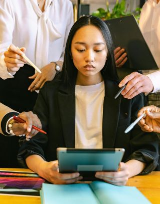 Focused young professional woman using a tablet amidst a busy office environment.