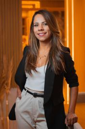 Portrait of a smiling businesswoman in elegant formalwear, captured indoors in a warm, modern setting.