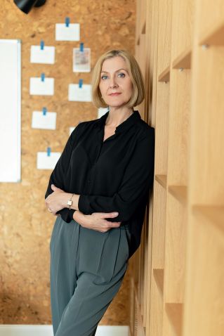 A confident mature woman stands in a modern office environment, exuding professionalism and elegance.